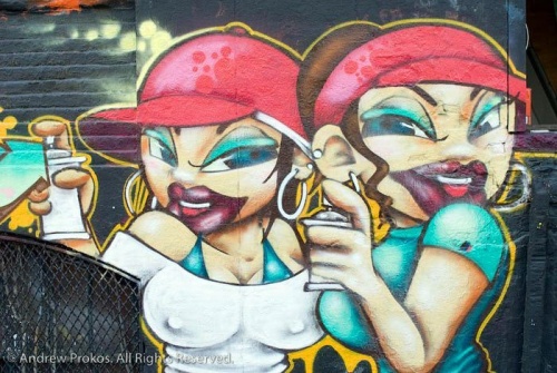 A street mural of girl graffiti artists with spray paint cans, Queens.