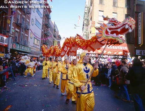 A street scene photo of men in costumes parading a dragon through Chinatown during the Chinese New Year parade, New York City