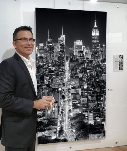 Photographer Andrew Prokos seen with a 60 inch print of his photo 'Vertical Cityscape of Manhattan at Night' in an art gallery exhibition