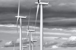 A black and white landscape photo of abandoned wooden farmhouse set among the enormous wind turbines of Biglow Canyon, Oregon.