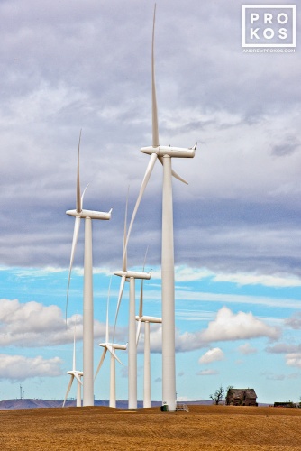 A landscape photo of massive wind turbines dwarfing an abandoned farmhouse at Biglow Canyon wind farm in Oregon