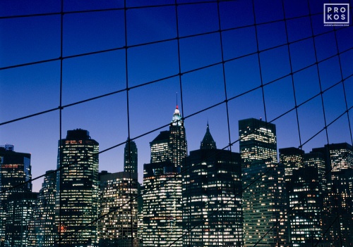 A view of Lower Manhattan as seen through the suspension cables of the Brooklyn bridge at night, New York City. Fine art prints of this photo are available framed in various styles.