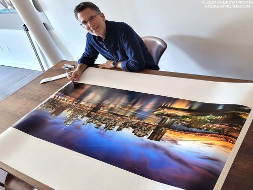 Photographer Andrew Prokos signing a sixty inch wide limited edition fine art photography print of a view of the Brooklyn Bridge and NYC at dusk