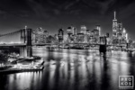 A long-exposure night view of the Brooklyn Bridge, East River, and Lower Manhattan skyline in black and white. Available as limited edition fine art prints framed in various styles.