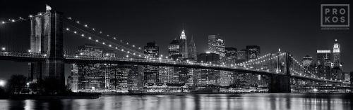 A panoramic skyline of the Brooklyn Bridge and Lower Manhattan at night in black and white
