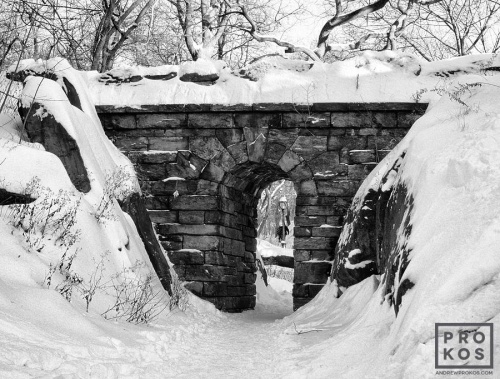 A black and white landscape photo of Central Park's Rustic Stone Arch under a blanket of Winter snow, New York City. Fine art prints of this photo are available up to 60 inches in width and framed in various wood, metal and acrylic styles.