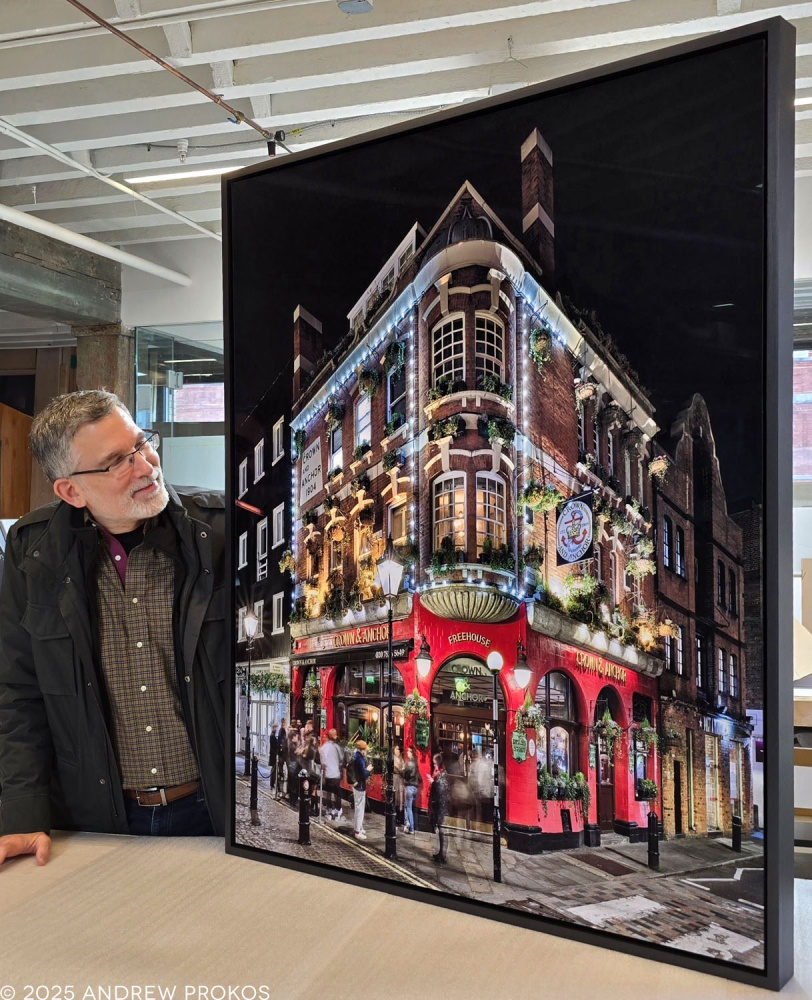 Photographer Andrew Prokos with a 50x42 inch framed limited edition print of Crown & Anchor pub in London as seen at night.