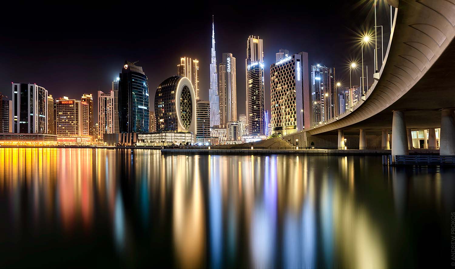 A large format photograph of the view of the Burj Khalifa and towers of Downtown Dubai at night as seen from Dubai Business Bay by photographer Andrew Prokos
