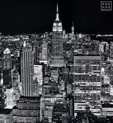 A high-definition black and white cityscape of the skyscrapers of Midtown Manhattan NYC and the Empire State Building as seen from from Rockefeller Center at night by photographer Andrew Prokos