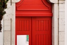 A fine art photo of a bright red door leading to a whitewashed courtyard in the Alfama neighborhood of Lisbon, Portugal