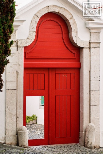 A fine art photo of a bright red door leading to a whitewashed courtyard in the Alfama neighborhood of Lisbon, Portugal