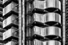 A black and white architectural view of the stainless steel clad exterior of the Lloyd's Building in London, by architect Richard Rogers.
