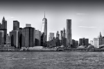 A black and white panoramic photograph of the Lower Manhattan skyline and the Brooklyn Bridge, New York