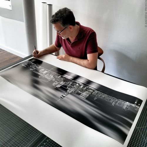 Black and white limited edition print of Panoramic Skyline of Lower Manhattan at Night being signed by photographer Andrew Prokos.