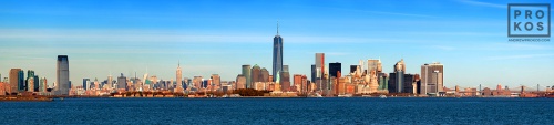 A panoramic skyline photo of New York City, World Trade Center, Statue of Liberty, and New York Harbor during the day.