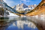 A high-definition landscape photo of the Maroon Bells mountain range in winter reflected on the frozen surface of Maroon Lake, near Aspen, Colorado.