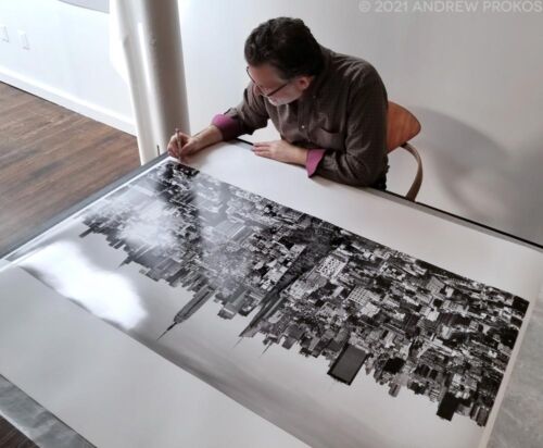 A large black and white cityscape photograph of Manhattan being signed by photographer Andrew Prokos