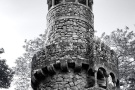 A black and white photo of the tower of the Poco Iniciatico, a hidden well with arched spiral stairway in the Quinta da Regaleira gardens of Sintra, Portugal