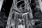 A black and white fine art photo of the Atlas statue at Rockefeller Center and St. Patrick's Cathedral at night, New York City.