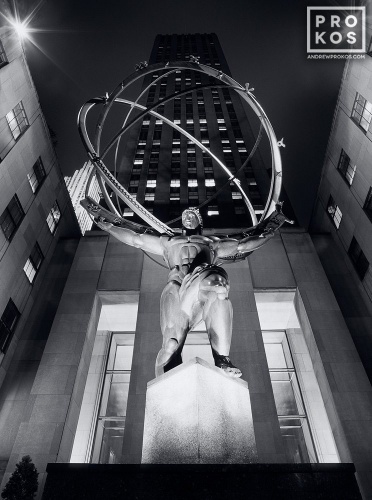 A black and white fine art photo of the famous Art Deco statue of Atlas at Rockefeller Center illuminated at night, New York City. Fine art prints of this photo are available framed in various styles. 
