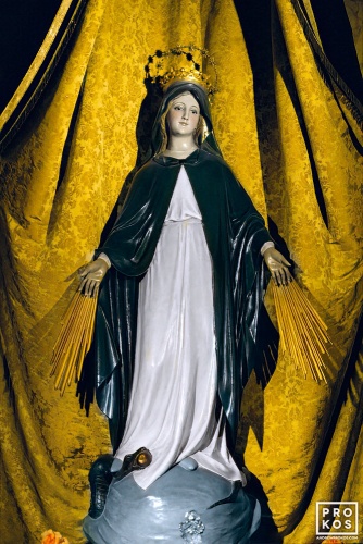 A painted statue of a Madonna with a gold crown of stars standing on a globe and set against a gold brocade canopy from a church in Madrid, Spain. Fine art prints of this photo are available framed in various styles, please inquire.