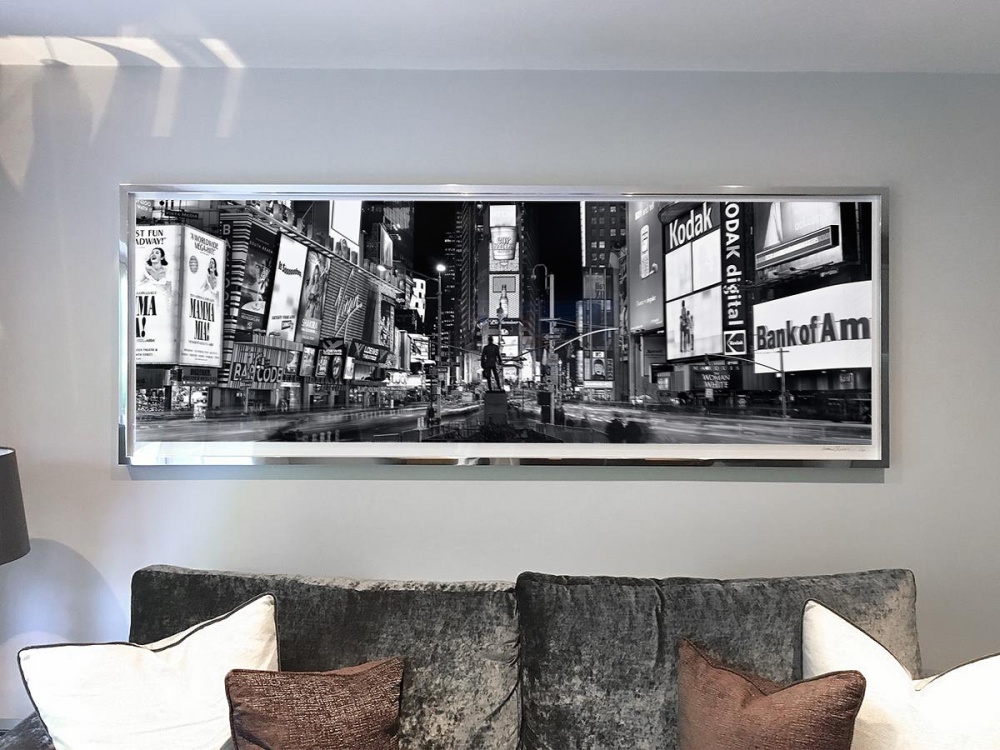 A 90 inch black and white print of "Panoramic View of Times Square at Night" by photographer Andrew Prokos framed in a high polish chrome frame.