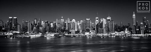 A black and white panoramic skyline photo of Midtown Manhattan at night from Weehawken, New Jersey.