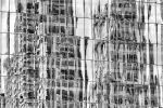 A black and white photograph capturing the reflections of the Woolworth Building and other towers of Lower Manhattan on a glass facade, New York City. Large-scale limited-edition prints of this photo are available up to 80 inches in height.