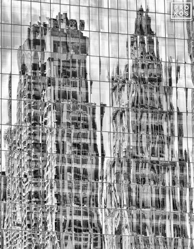 A black and white photograph capturing the reflections of the Woolworth Building and other towers of Lower Manhattan on a glass facade, New York City. Large-scale limited-edition prints of this photo are available up to 80 inches in height.